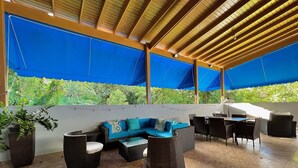 An outdoor patio area with a blue canopy, wicker furniture, and potted plants. - Luxury Villa with Pool, Heated Jacuzzi, & Terrace in El Yunque Rainforest (Río Grande)
