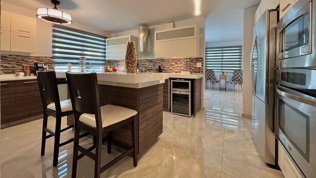 A modern kitchen with a central island, dark wooden chairs, a built-in oven, and stainless steel appliances. - Luxury Villa with Pool, Heated Jacuzzi, & Terrace in El Yunque Rainforest (Río Grande)
