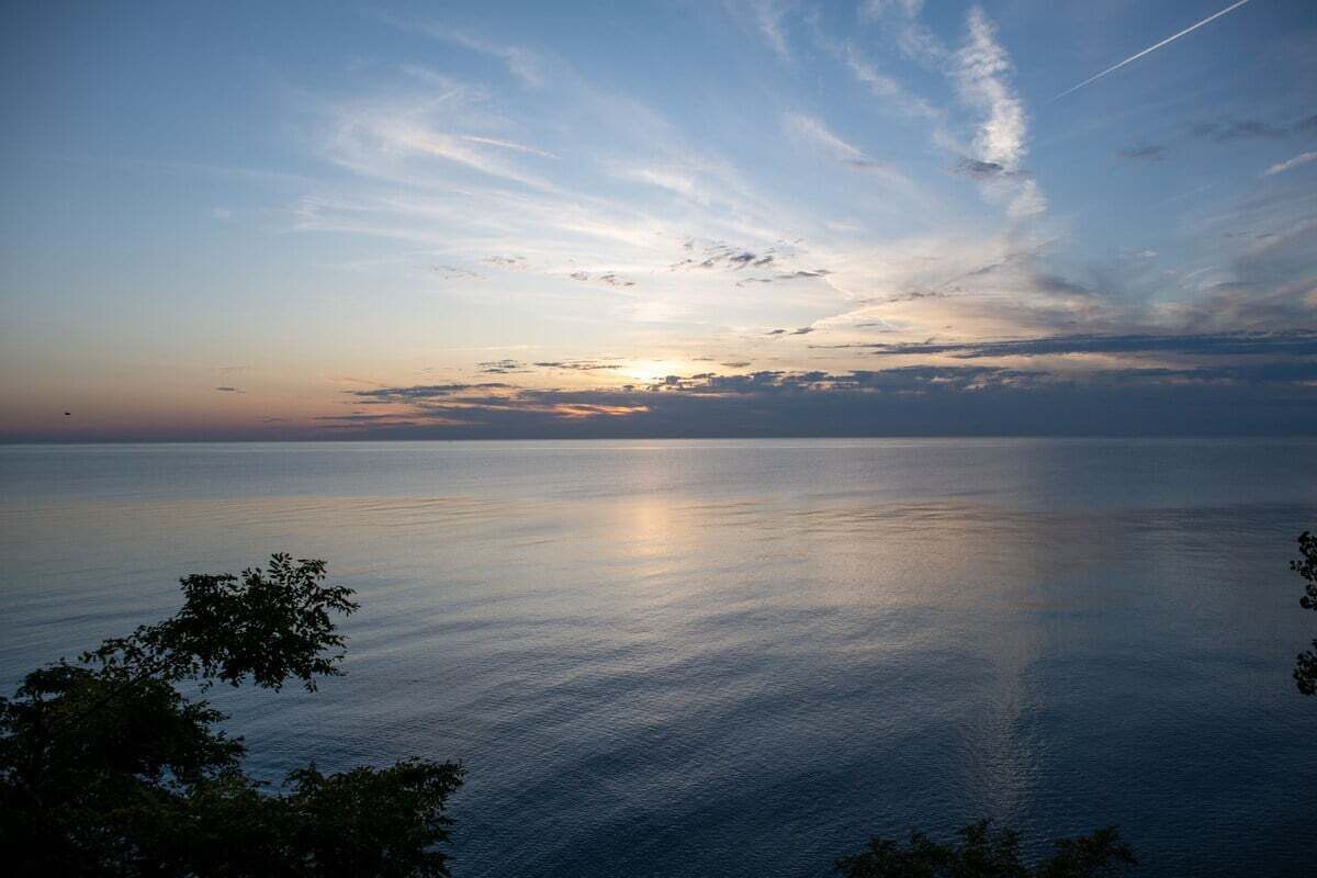 Tyyni meri auringonlaskun aikaan, taivas on kirkas ja siellä on vain muutama pilvi.