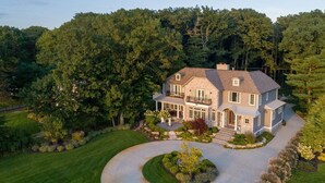 A large, two-story house with a spacious driveway, surrounded by lush greenery and trees. - Luxurious 6 bedroom estate with lake view & beach (Fennville)