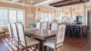 A spacious kitchen with a central island, pendant lighting, and a dining area with a large wooden table and upholstered chairs. - Luxurious 6 bedroom estate with lake view & beach (Fennville)
