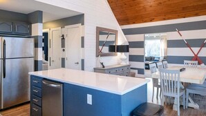 A modern kitchen with a central island, stainless steel appliances, and a wooden ceiling.