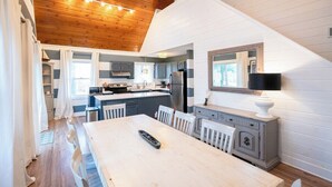A modern kitchen with white cabinetry, a dining area with a white table, and a wooden ceiling.