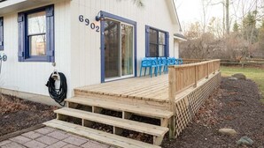 A white building with the number 6902, a wooden deck with blue chairs, and a hose on the side.