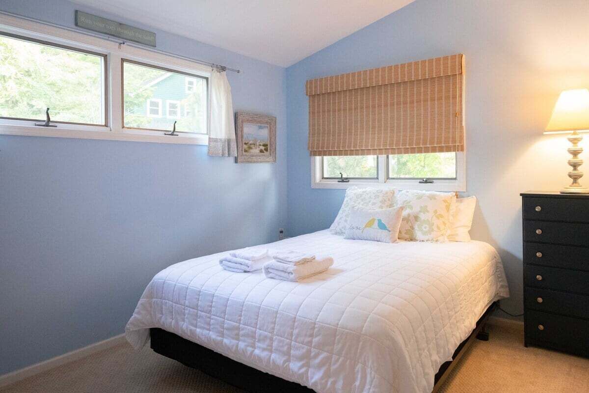 Ein Schlafzimmer mit Bett, Schminktisch, zwei Fenstern mit Vorhängen und einer Lampe.