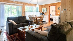 A cozy living room with a sofa, coffee table, and dining table. There is a kitchen area with a refrigerator and a sink. - Updated Cozy Cabin near Lake Michigan (Holland)
