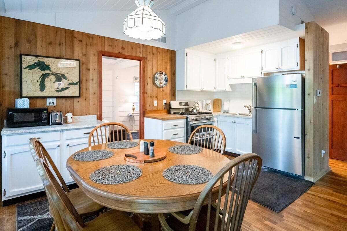 A compact kitchen with white cabinets, a stainless steel refrigerator, and a wooden dining table with placemats.