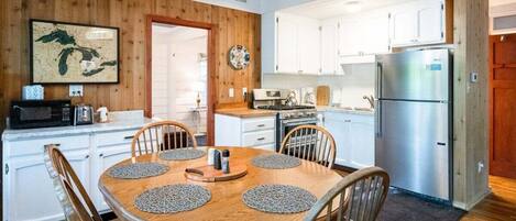 A compact kitchen with white cabinets, a stainless steel refrigerator, and a wooden dining table with placemats.