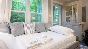 A bedroom with a large bed, multiple pillows, a door with a window, and a view of trees outside. - Updated Cozy Cabin near Lake Michigan (Holland)