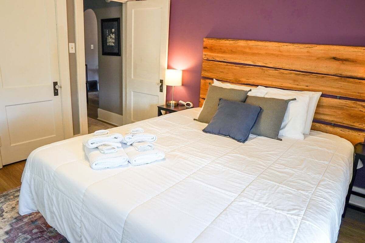 A neatly made bed with white linens and a wooden headboard, a bedside lamp, and a door leading to another room.