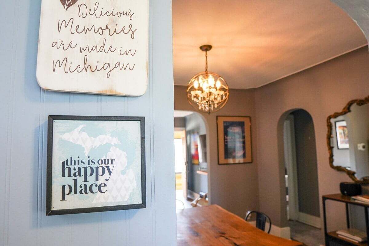 A dining area with a wooden table and chairs, a chandelier, and two framed signs on the wall.