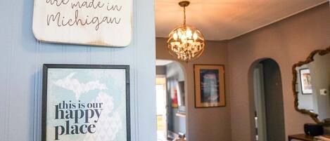 A dining area with a wooden table and chairs, a chandelier, and two framed signs on the wall.