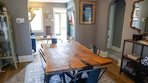 A dining area with a wooden table and blue chairs, a rug, and a bookshelf with books and a speaker.