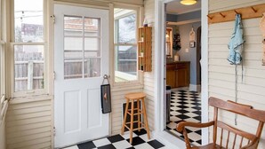 A hallway with a white door, a wooden stool, a wooden chair, and a checkered floor.
