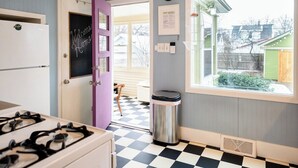 A kitchen with a checkered floor, a refrigerator, a stove, a trash can, and a window with a view of the outside.