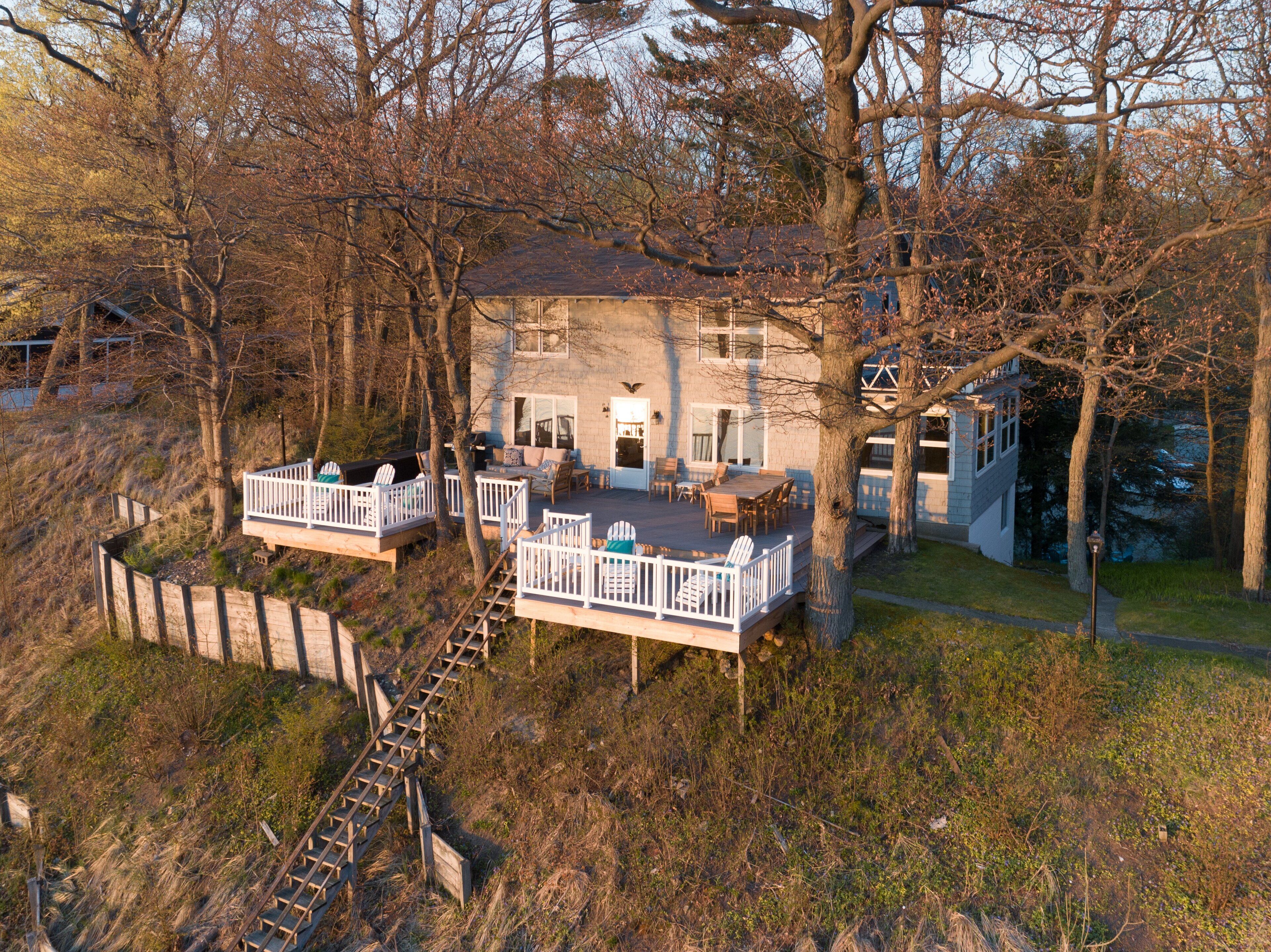Une maison à deux étages dotée d’une terrasse, d’un escalier et offrant une vue sur les arbres environnants.