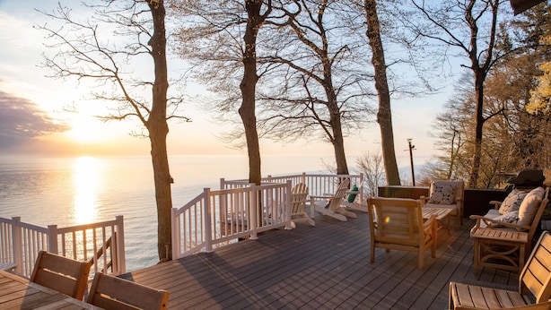 A wooden deck with seating and a railing overlooking a body of water during sunset. - Classic Lake MI Cottage w/Beach and Incredible Views (West Olive)