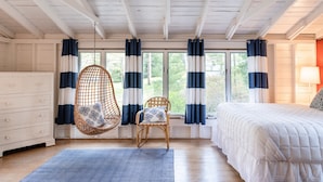A room with a bed, a hanging chair, a chair with a patterned cushion, a dresser, and a window with curtains. - Classic Lake MI Cottage w/Beach and Incredible Views (West Olive)