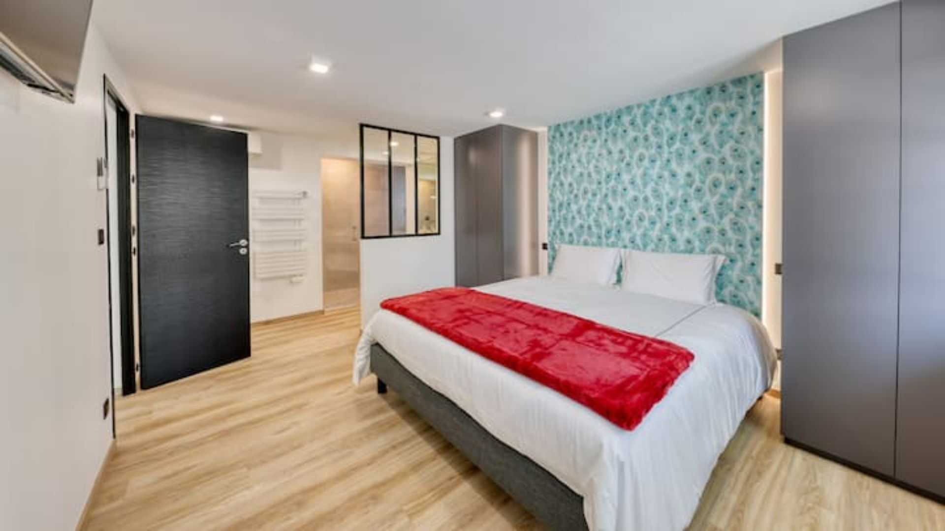 Une chambre moderne avec un lit, une couverture rouge, une armoire et un mur à motifs.