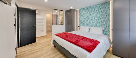 Une chambre moderne avec un lit, une couverture rouge, une armoire et un mur à motifs.