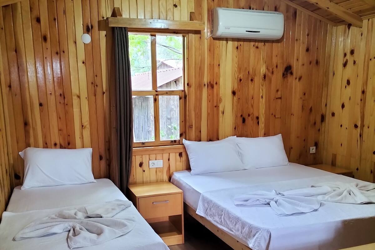 A wooden cabin room with two beds, a nightstand, and an air conditioning unit.