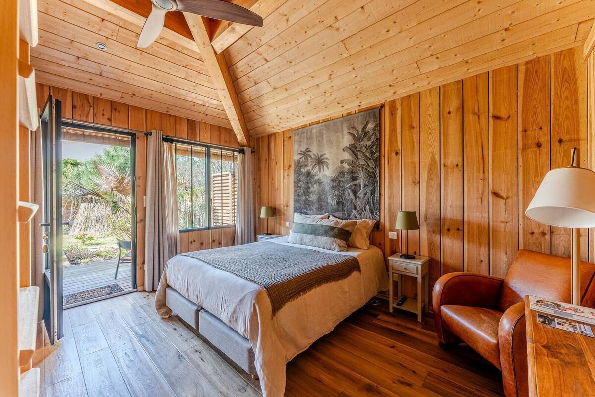 A wooden cabin bedroom with a bed, two bedside tables, a chair, and a mural on the wall.