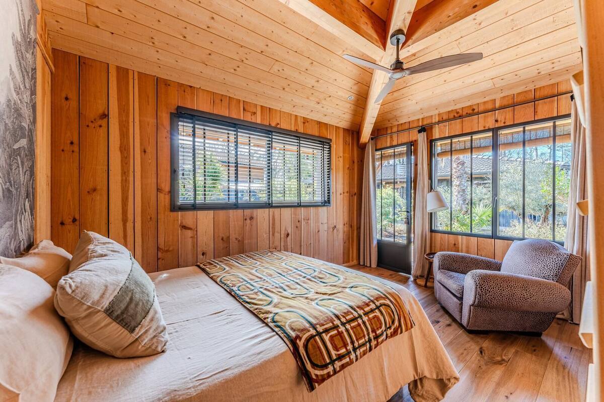 A wooden cabin bedroom with a bed, a chair, and large windows.