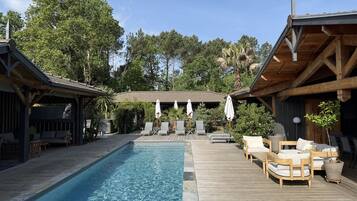 Un espace piscine doté d’une terrasse en bois, de chaises longues et de parasols.