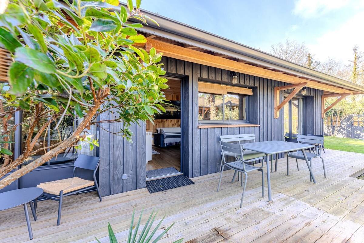 A modern outdoor patio with a wooden deck, metal furniture, and a view into the house.