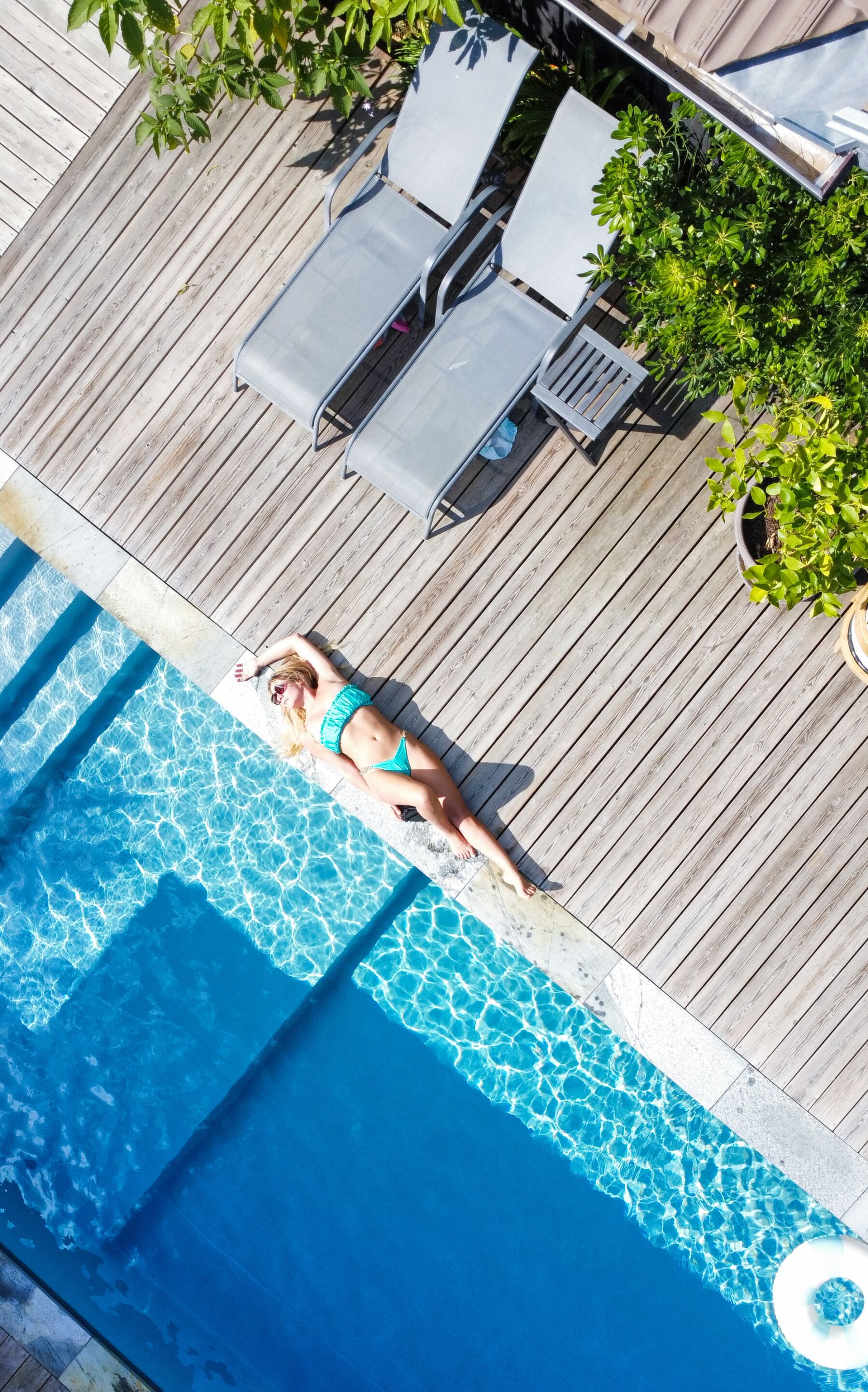 Un espace piscine doté d’une terrasse en bois, de chaises longues et d’une personne se relaxant au bord de la piscine.