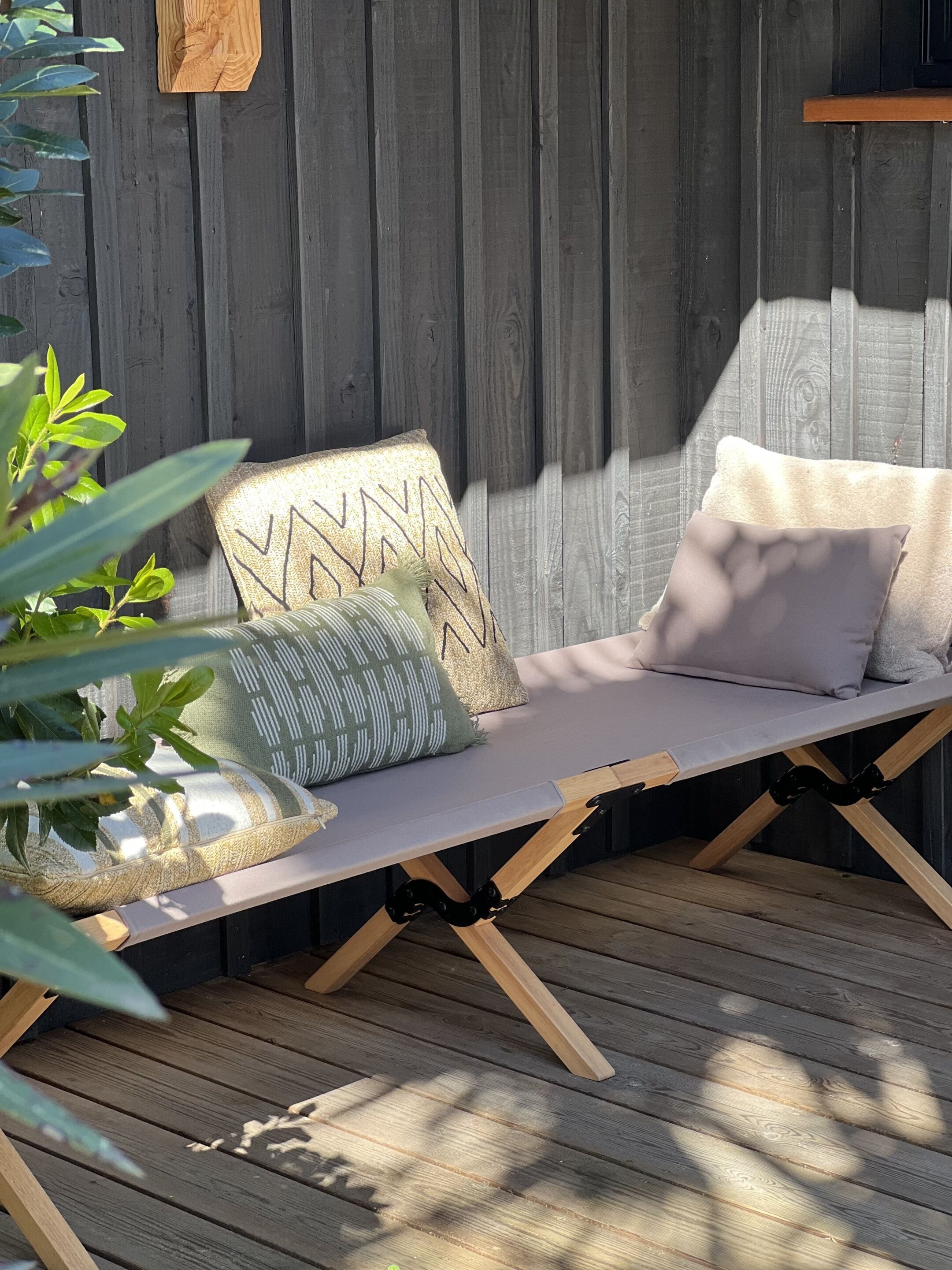 Une terrasse en bois avec un banc rembourré, un panier tressé et une plante en pot.
