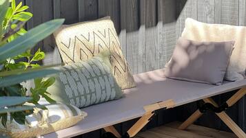 Une terrasse en bois avec un banc rembourré, un panier tressé et une plante en pot.