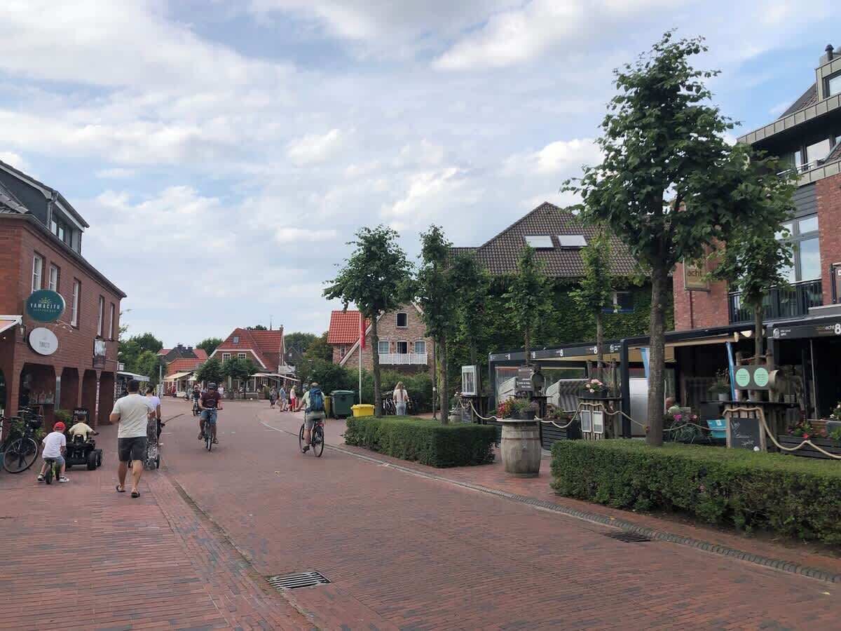 Eine Fußgängerzone mit Gebäuden, einige mit sichtbaren Schildern, und Menschen, die gehen und Fahrrad fahren.