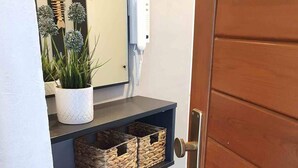 En trädør med metalgreb, en hvid væg med et indrammet spejl, en potteplante og fletkurve på en hylde.
