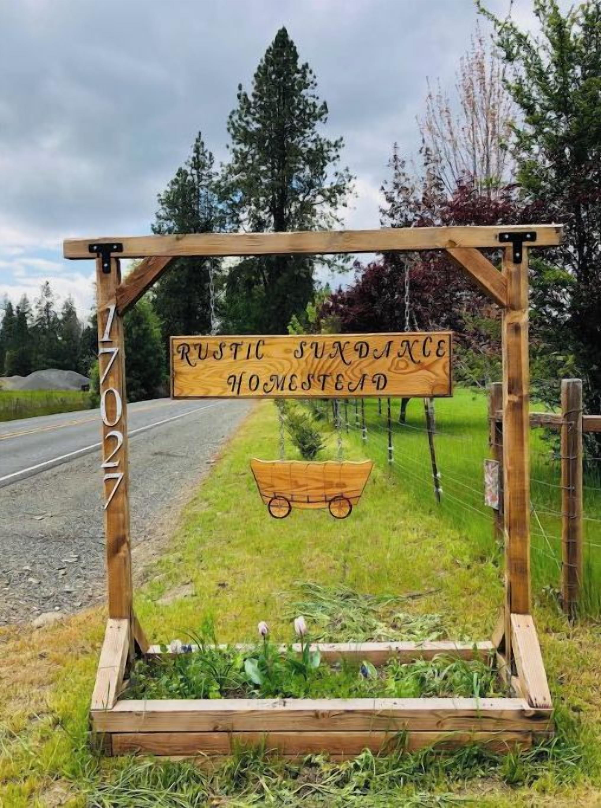 Et rustikt træskilt med teksten "Rustic Sundance Homestead" og et vognhjul.