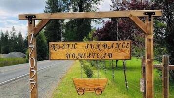 Et rustikt træskilt med teksten "Rustic Sundance Homestead" og et vognhjul.