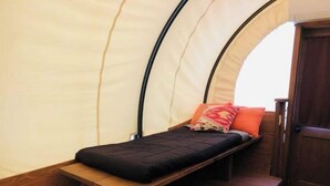 A tent with a single bed, a bench, and a door.