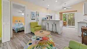 A compact room with a bed, a green armchair, a round table, and a kitchenette.