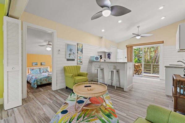 A compact room with a bed, a green armchair, a round table, and a kitchenette.