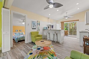 A compact room with a bed, a green armchair, a round table, and a kitchenette. - The Palms Cottage One- A Green Haven on Sanibel (Sanibel)
