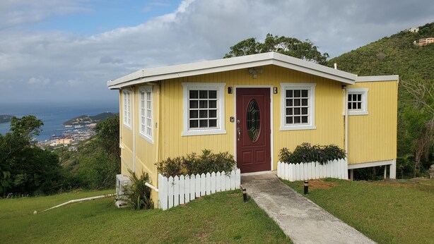 A small yellow building with a red door, white picket fence, and a concrete path leading to the entrance. - Villa Rose (Charlotte Amalie)