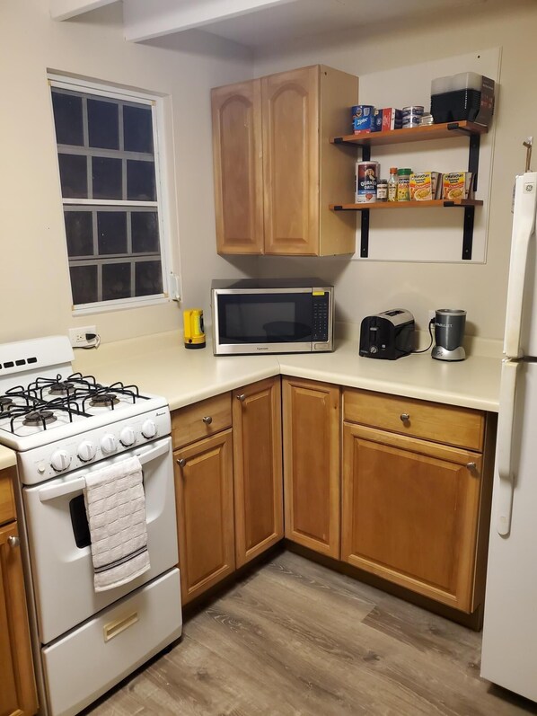 A kitchen with wooden cabinets, a microwave, a stove, and a shelf with food items.