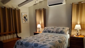 A bedroom with a bed, two bedside tables, an air conditioning unit, and curtains. - Villa Rose (Charlotte Amalie)