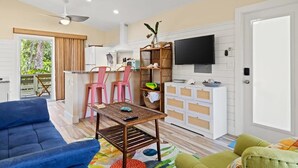 Un salon comprenant un canapé, une table basse, un téléviseur et un coin cuisine avec des chaises et un comptoir.