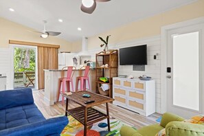 Ein Wohnzimmer mit Sofa, Couchtisch, Fernseher und Küchenzeile mit Stühlen und einer Theke.