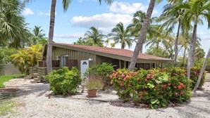 Un bâtiment d’un seul étage, avec un toit rouge, entouré de palmiers et de plantes tropicales.