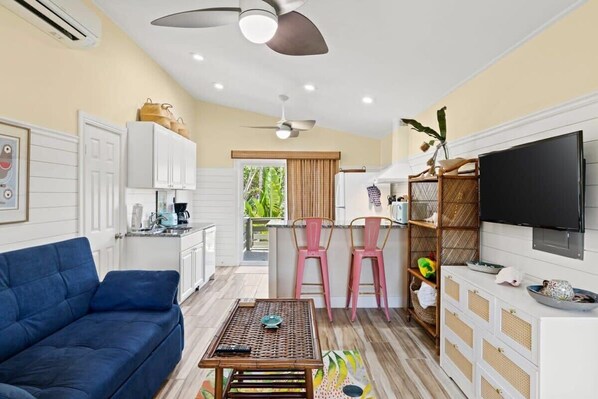 A living room with a sofa, a coffee table, a TV, and a kitchen area with a counter and chairs.