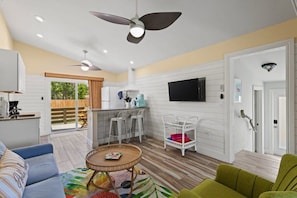 Un vaste espace de vie comprenant un ventilateur de plafond, une table à manger, un canapé et un téléviseur fixé au mur.