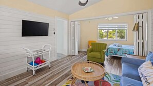 Una habitación con ventilador de techo, televisor, un sillón verde, un sofá azul y una mesita con un libro.