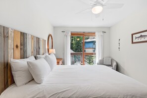 Una camera da letto con un letto, una testata imbottita in legno, una ventola a soffitto, una finestra con tende e un quadro di pesci appeso al muro.